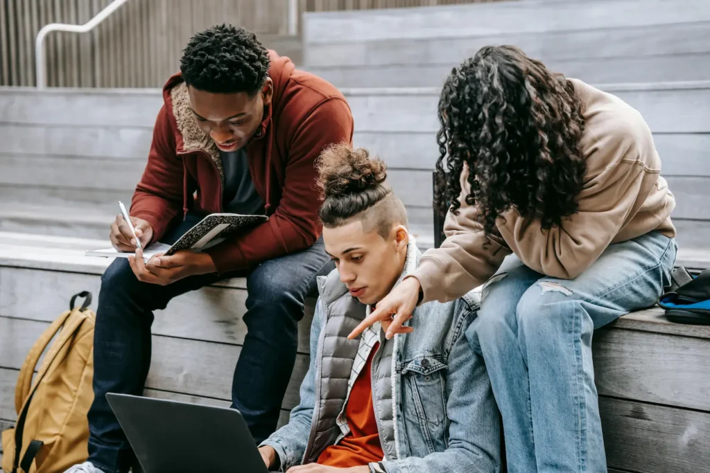Students collaborate on outdoor steps, with one using a laptop and others sharing notes for a group study task.